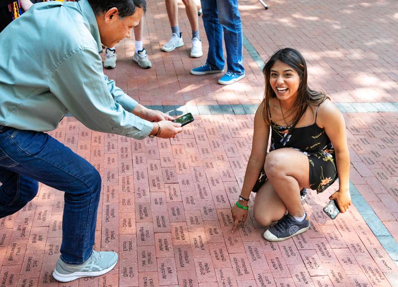 student points to a brick that has their named engraved on a walkway